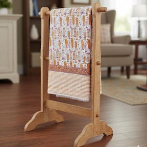 Peut inclure: Un porte-serviettes en bois avec un textile à motifs. Le textile présente un fond blanc avec des motifs de poissons orange, roses et bruns. Le support est en bois clair et a un design simple.