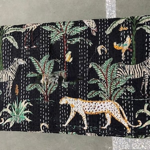 May include: Black kantha quilt featuring a repeating pattern of zebras, leopards, and palm trees. The quilt is made from cotton and has a hand-stitched design.