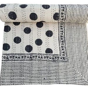 May include: A cream-colored cotton quilt featuring a black polka dot pattern on the main section, bordered by a thin floral band and a striped edge. The fabric displays visible running stitch quilting details throughout the entire surface.