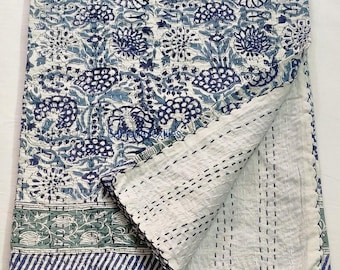 May include: A white cotton kantha quilt with a blue and green floral pattern. The quilt is folded in half and has a white backing with a small stitch pattern.