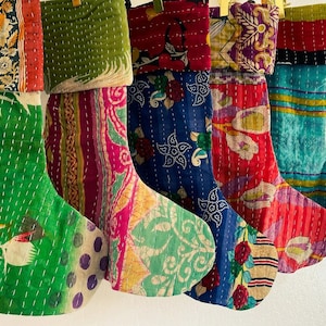 Op de afbeelding: Vijf kleurrijke kerstsokken gemaakt van hergebruikt materiaal. De sokken zijn versierd met bloemenpatronen en strepen in tinten groen, blauw, rood, roze en paars.