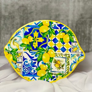 May include: A lemon-shaped serving board with a bright design. The board has a yellow edge and a colourful pattern of lemons, green leaves, and blue and white tiles. It is a decorative item for the kitchen.