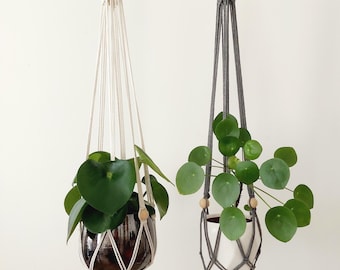 May include: Two macrame plant hangers with wooden beads, one white and one gray, each holding a potted plant with green leaves.