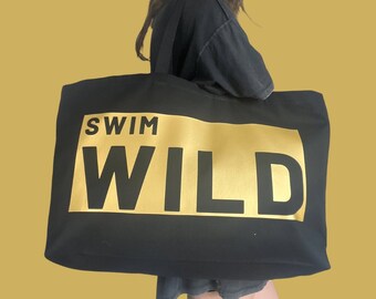 May include: Black tote bag with a gold rectangle that says "Swim Wild" in black letters.