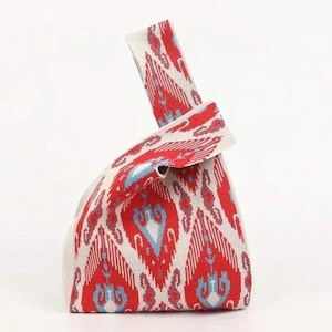 Könnte beinhalten: Eine Stoffknotentasche mit rotem, weißem und blauem Muster. Die Tasche hat ein sich wiederholendes Ikat-Design. Der Griff ist oben verknotet. Die Tasche besteht aus einem gewebten Material.
