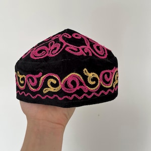 Può includere: Berretto in velluto nero con motivi a vortice ricamati in rosa e oro. Il berretto ha una corona arrotondata e una fascia decorativa alla base. Il ricamo è dettagliato e aggiunge un tocco di eleganza.
