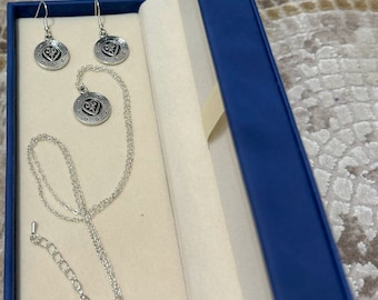May include: A silver necklace and earrings set with a heart-shaped pendant and matching earrings. The pendant and earrings feature a detailed design with a heart in the center and a circle of small dots around the edge.