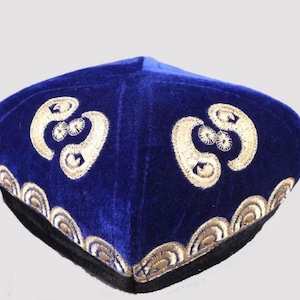 Può includere: Un cappello di velluto blu con ricami dorati. Il cappello presenta un disegno geometrico sulla corona e un bordo decorativo. Il cappello ha un bordo nero ed è probabilmente un oggetto culturale tradizionale.