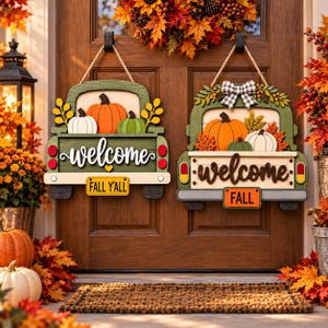 May include: Two wooden door signs shaped like vintage trucks, both featuring the word welcome in script. The left sign is green with orange and white pumpkins and a yellow license plate reading FALL Y'ALL. The right sign has a plaid bow.