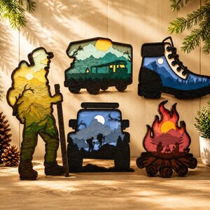 Peut inclure: Un ensemble de cinq décorations murales en bois superposé sur le thème de la randonnée : un randonneur, un camping-car, une chaussure de marche, une silhouette de véhicule avec des montagnes et un feu de camp, avec des découpes détaillées.