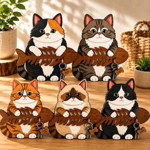 May include: Five wooden cat-shaped key holders, each featuring a different feline coat pattern and color. Each cat holds a dark brown wooden fish skeleton in its paws, which serves as a hook for a metal keyring with a small bone-shaped name tag.