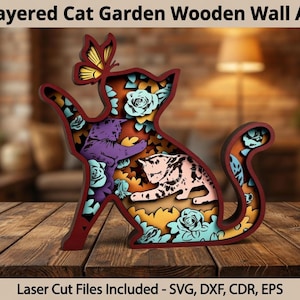 May include: Layered wooden wall art in the shape of a cat, featuring a butterfly and two cats inside. The design includes floral accents and is made of layered wood. The text "Layered Cat Garden Wooden Wall Art" is at the top.