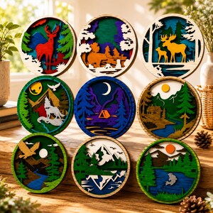 May include: A collection of nine circular wooden wall art pieces featuring layered, laser-cut nature scenes. Designs include a red deer, a moose with calf, a howling wolf, a camping tent under a crescent moon, a cabin, an eagle, and a jumping fish.