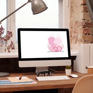 Puede incluir: Un monitor de ordenador con un dise&ntilde;o floral rosa y blanco en la pantalla. El monitor est&aacute; sobre un escritorio de madera con una l&aacute;mpara, una planta en maceta, un teclado, un rat&oacute;n, unas gafas, un cuaderno, un bol&iacute;grafo y una taza.
