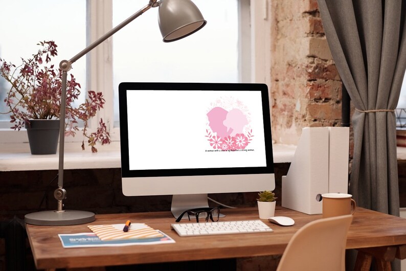 Puede incluir: Un monitor de ordenador con un dise&ntilde;o floral rosa y blanco en la pantalla. El monitor est&aacute; sobre un escritorio de madera con una l&aacute;mpara, una planta en maceta, un teclado, un rat&oacute;n, unas gafas, un cuaderno, un bol&iacute;grafo y una taza.