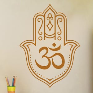 Può includere: Una mano di hamsa marrone con dettagli intricati e un simbolo Om al centro. La hamsa è un simbolo di protezione e buona fortuna.