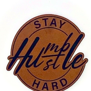 May include: A brown leather patch with the text "Stay Humble Hustle Hard" in black lettering.
