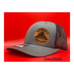 May include: A grey and black trucker hat with a brown leather patch that says "We Keep It Rolling".