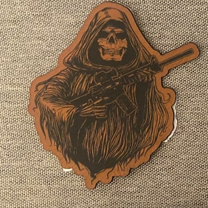 May include: A brown leather sticker with a black and white illustration of a hooded skeleton holding a rifle.