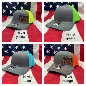 May include: Four trucker hats with a gray crown and a mesh back. The hats have a brown leather patch with the word "DAD" on the front. The mesh back is available in four colors: yellow, green, blue, and orange.