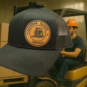 May include: Black trucker hat with a mesh back and a circular patch that reads "Certified Forklift Operator." The patch features a forklift graphic. The hat is worn by a person operating a forklift.