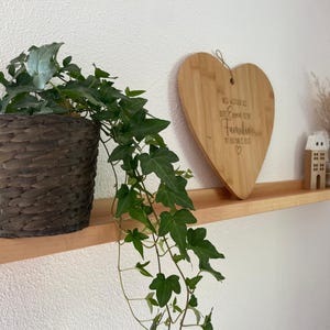 Op de afbeelding: Een houten plank met een hartvormig snijplank waarop staat "We may not be perfect but we are each other's family" en een plant in een pot met groene bladeren.