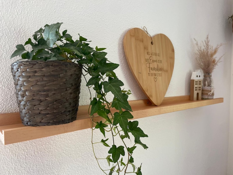 Op de afbeelding: Een houten plank met een hartvormig snijplank waarop staat "We may not be perfect but we are each other's family" en een plant in een pot met groene bladeren.