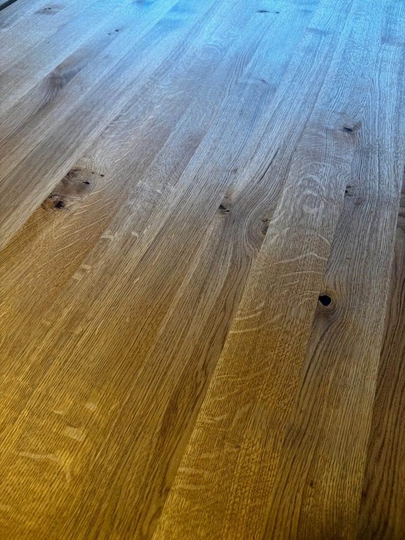 May include: Close-up of a wooden surface with a natural wood grain pattern. The wood has a warm, golden-brown hue with darker knots and variations in color. The planks are arranged in parallel lines, creating a textured and visually appealing surface.
