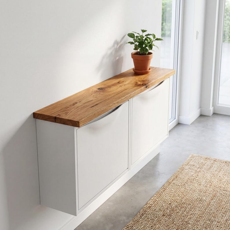 May include: A white cabinet with a natural wood top and curved metal handles. A small potted plant sits on top of the cabinet. The cabinet is mounted on a white wall.