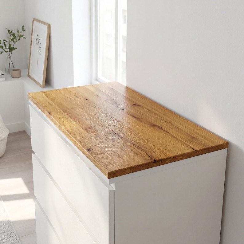 May include: A white dresser with a light brown wooden top. The wood grain is visible on the top surface. The dresser has four drawers and is positioned near a window.