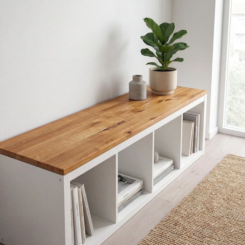 May include: A white storage bench with a natural wood top. The bench has four cubby spaces filled with books and decorative items. A potted plant and a small vase sit on top of the bench.