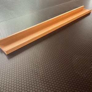 Op de afbeelding: Een houten plank met een eenvoudig ontwerp, perfect voor het tentoonstellen van kleine voorwerpen. De plank is gemaakt van natuurlijk hout en heeft een lichtbruine kleur.