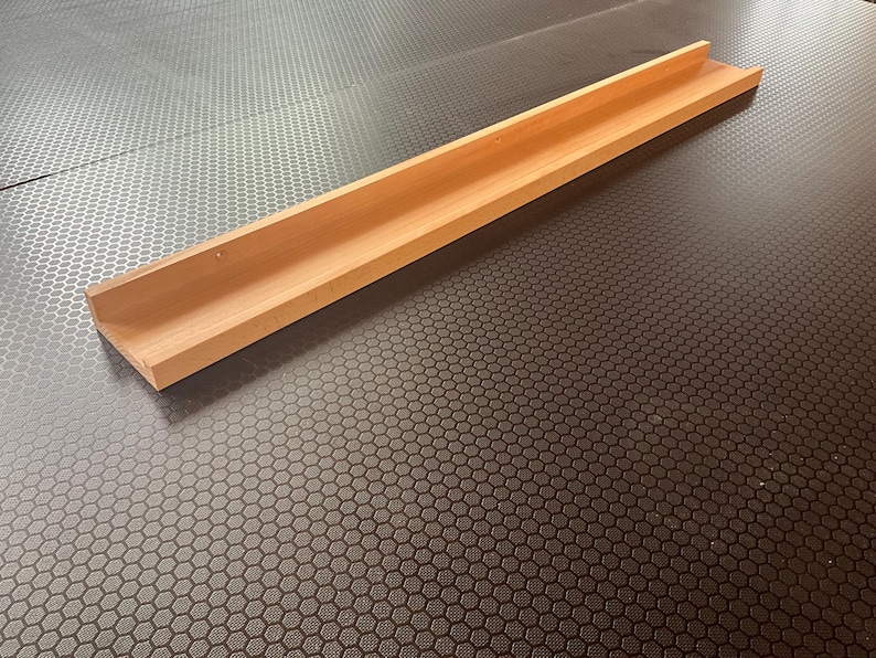 Op de afbeelding: Een houten plank met een eenvoudig ontwerp, perfect voor het tentoonstellen van kleine voorwerpen. De plank is gemaakt van natuurlijk hout en heeft een lichtbruine kleur.