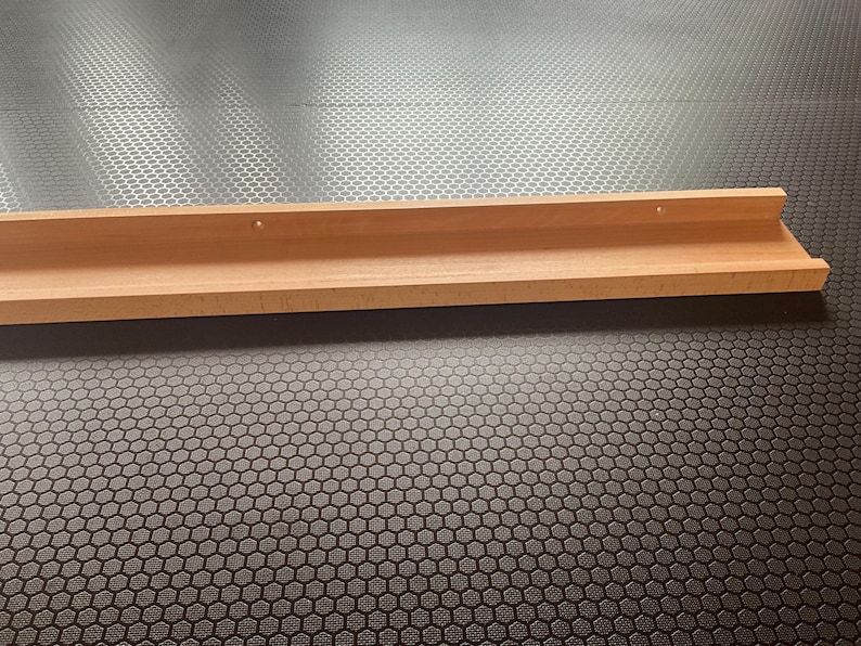 Op de afbeelding: Een houten plank met een lichte bocht aan de voorkant. De plank is lichtbruin en heeft twee kleine gaatjes aan de bovenkant.