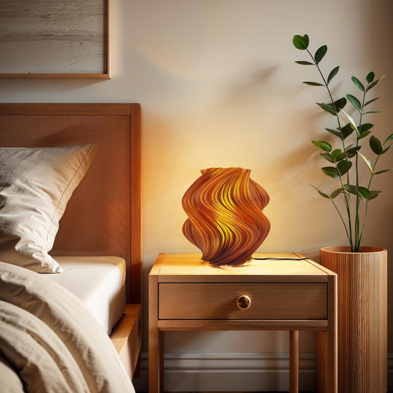 May include: A table lamp with a spiraling, wave-like structure featuring a gradient of warm orange, yellow, and brown tones. The lamp emits a soft, glowing light from within, casting a warm illumination across the surface it rests upon.