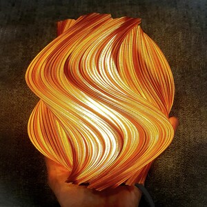 May include: A 3D printed lamp with a swirling, wave-like structure that glows with a warm orange and yellow light. The surface features intricate, vertical ridges that create a dynamic, flame-like appearance, emitting a soft, diffused illumination.