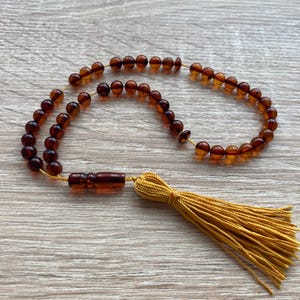 Può includere: Un mala di preghiera in ambra marrone con un fiocco giallo. Le perle sono rotonde e infilate su un filo sottile. Il fiocco è fatto di un materiale morbido e setoso.