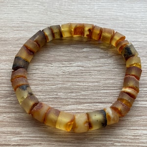 May include: A bracelet made of amber beads. The beads are a mix of light and dark amber, and some have a cloudy appearance. The bracelet is on a wooden surface.