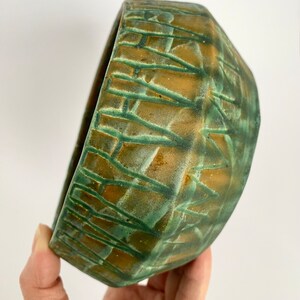 Może przedstawiać: Zielona i brązowa ceramiczna miska z geometrycznym wzorem. Miska jest ręcznie robiona i ma unikalny, rustykalny wygląd.