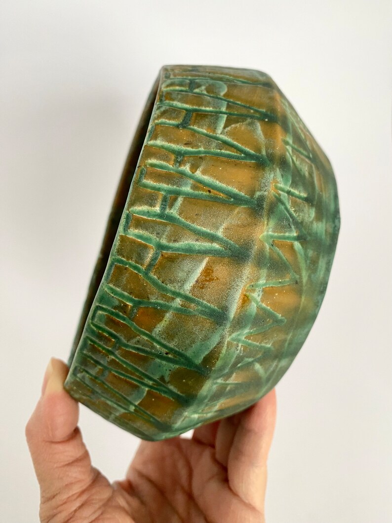 Może przedstawiać: Zielona i brązowa ceramiczna miska z geometrycznym wzorem. Miska jest ręcznie robiona i ma unikalny, rustykalny wygląd.