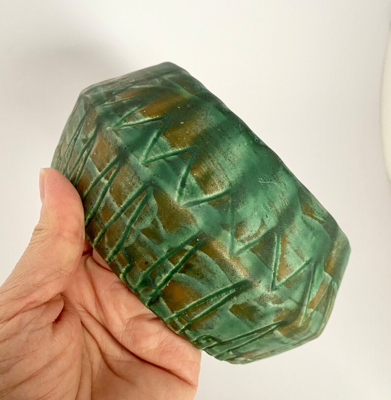Może przedstawiać: Zielona ceramiczna doniczka z geometrycznym wzorem w kolorze brązowym. Doniczka ma zaokrąglony kształt i fakturowaną powierzchnię.
