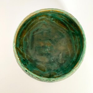 Może przedstawiać: Zielona ceramiczna miska z fakturowanym brzegiem. Miska ma marmurkową zielono-brązową glazurę.