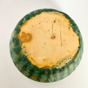 Może przedstawiać: Zielona, glazurowana ceramiczna miska z ż&oacute;łtym rantem i znakiem producenta na spodzie, kt&oacute;ry brzmi "M.T. 1912".
