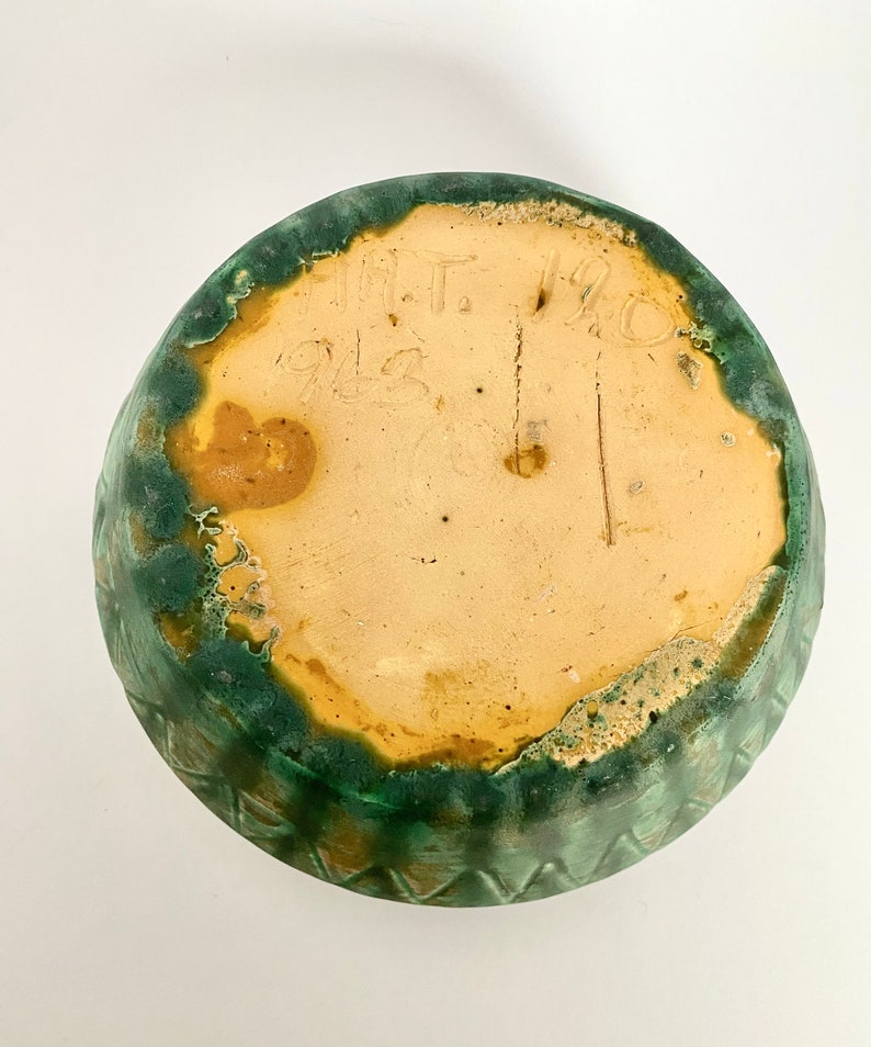Może przedstawiać: Zielona, glazurowana ceramiczna miska z ż&oacute;łtym rantem i znakiem producenta na spodzie, kt&oacute;ry brzmi "M.T. 1912".