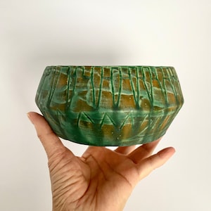 Op de afbeelding: Een groene en bruine keramische plantenpot met een geometrisch ontwerp. De pot heeft een brede, ronde basis en een licht uitlopende rand.