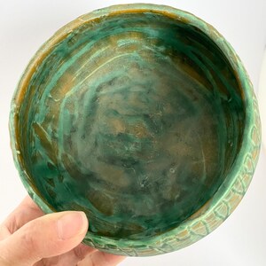 Może przedstawiać: Zielona i brązowa ceramiczna miska z fakturowanym zewnętrzem. Miska ma szeroki, okrągły kształt i gładkie wnętrze.