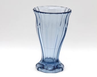 May include: A vintage-style, light blue glass sundae or parfait glass. The glass has a fluted design and a flared rim. The base is hexagonal. The glass is empty and sits against a white background.