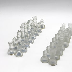 Könnte beinhalten: Ein Satz transparenter Glasschachfiguren, angeordnet in zwei Reihen. Die Figuren sind alle in verschiedenen Formen und Größen und alle aus klarem Glas.