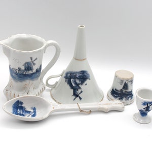 May include: A collection of white ceramic kitchenware with blue windmill designs. Includes a pitcher, funnel, spoon, thimble, and egg cup. The items have a rustic, hand-painted aesthetic.
