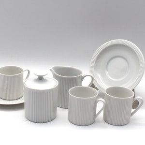 May include: White porcelain tea set with a sugar bowl, creamer, two cups and saucers. The cups and saucers have a ribbed design.